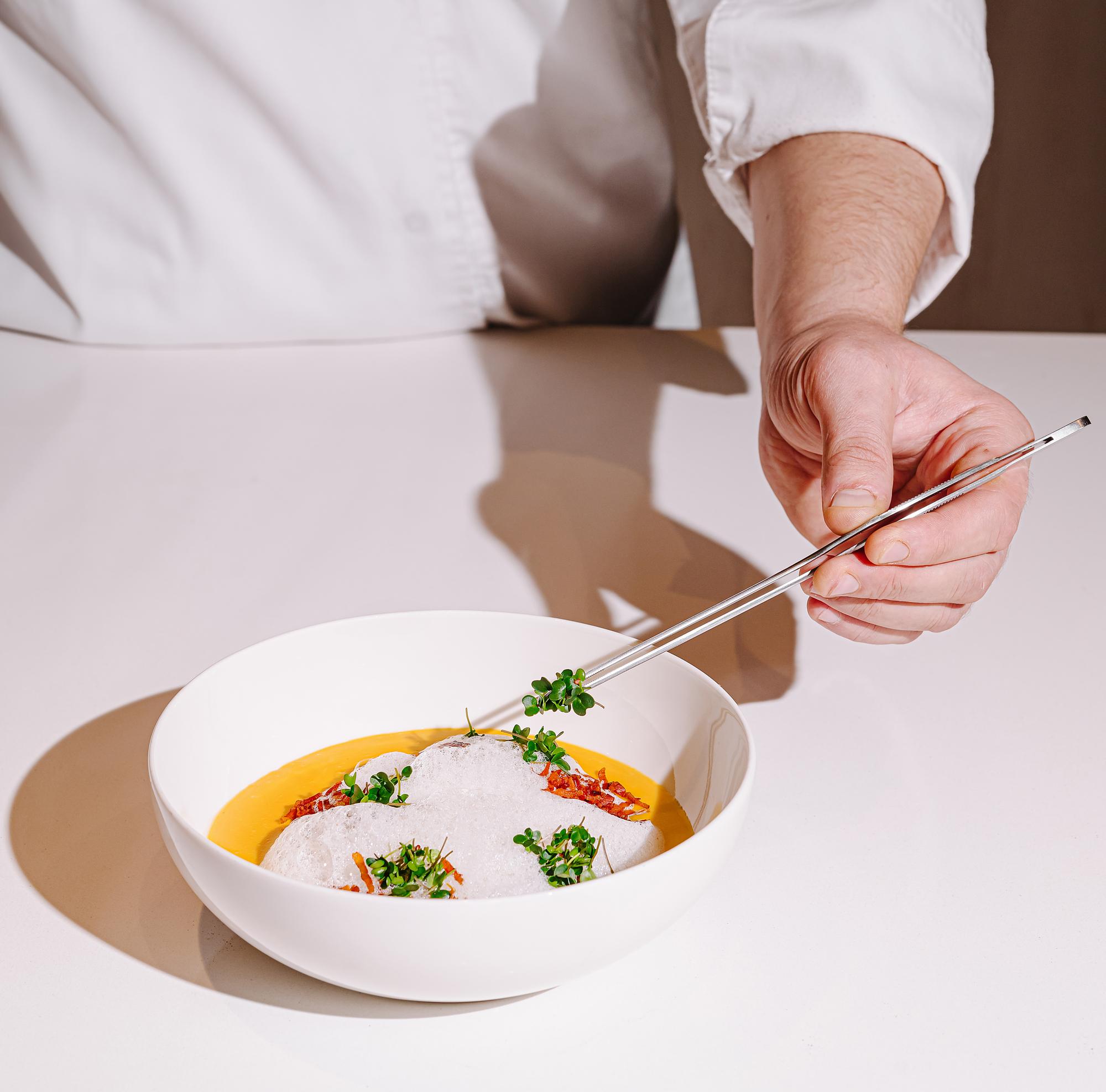 Chef plating with tweezers over neutral background